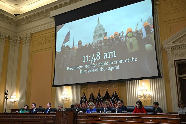 Una pantalla gigante muestra una imagen de hombres con sombreros naranjas frente al Capitolio de los Estados Unidos.